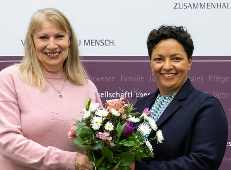 Staatsministerin Petra Köpping und Landestierschutzbeauftragte Carina Heinrich lächeln in die Kamera. Dabei halten sie einen Blumenstrauß