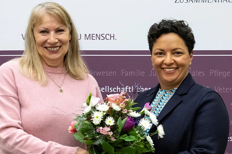 Staatsministerin Petra Köpping und Landestierschutzbeauftragte Carina Heinrich lächeln in die Kamera. Dabei halten sie einen Blumenstrauß